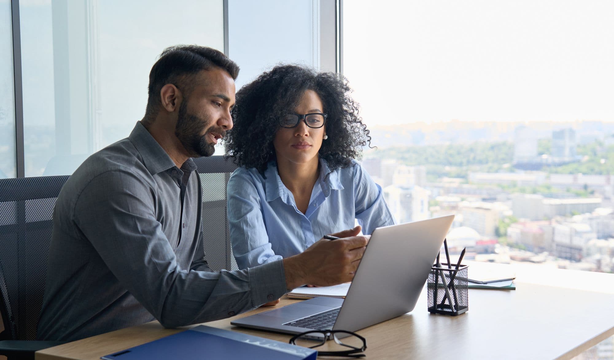 Two colleagues work through a laptop together at an office desk