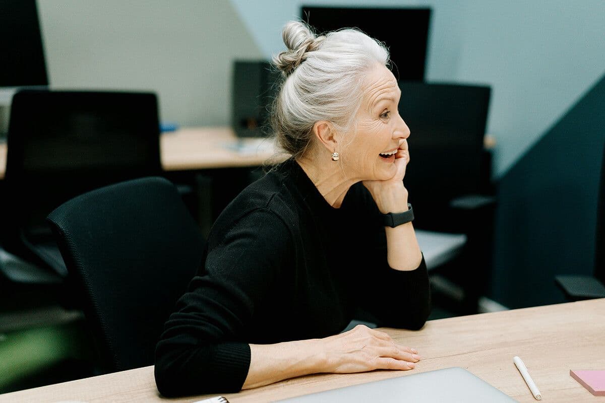Older woman in black sweater sitting at a conference table reacting to what her colleague just said.