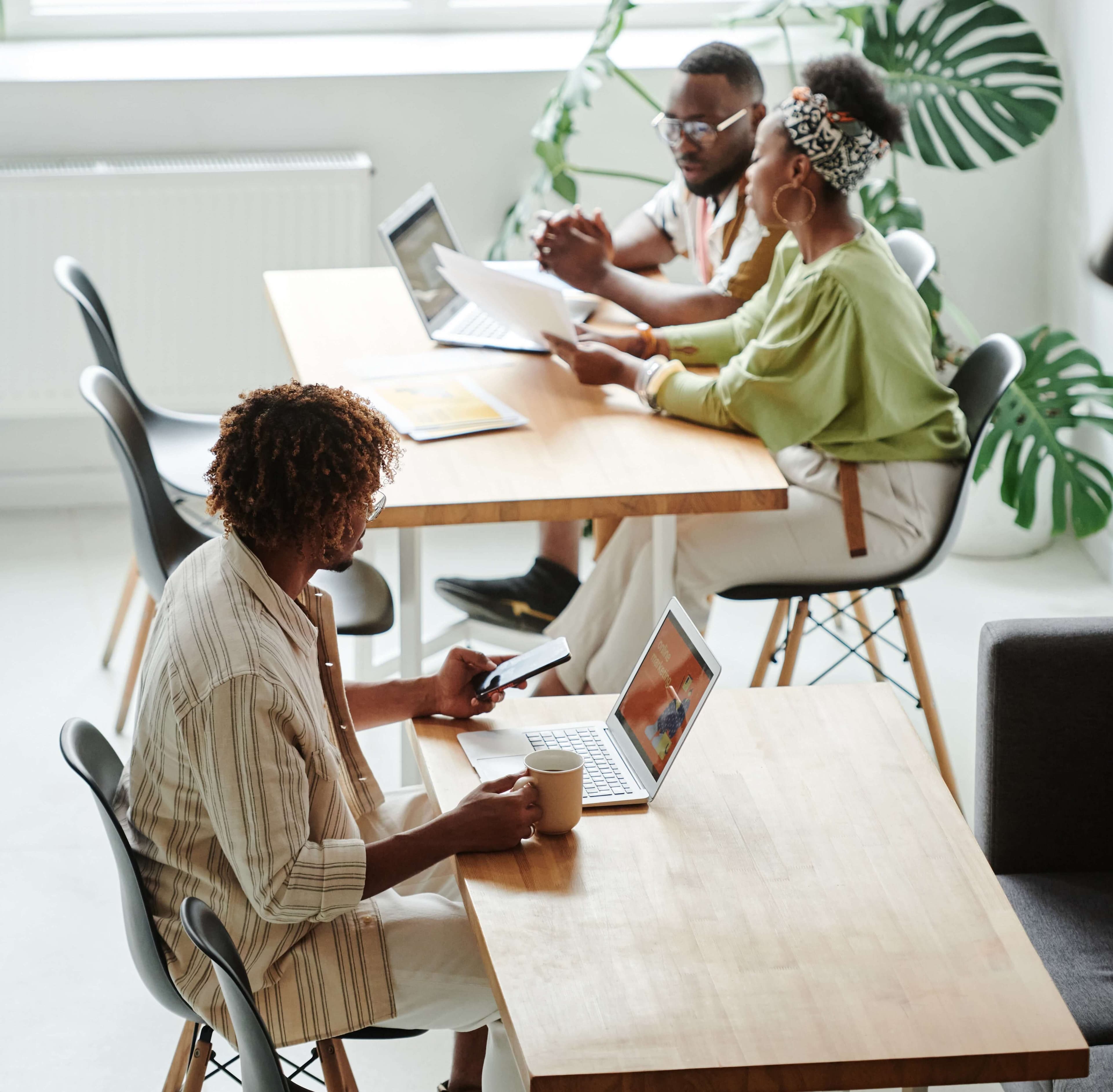 workplace mentorship meeting between Black female employee and Black male employee. Other Black male employee sits at another table.