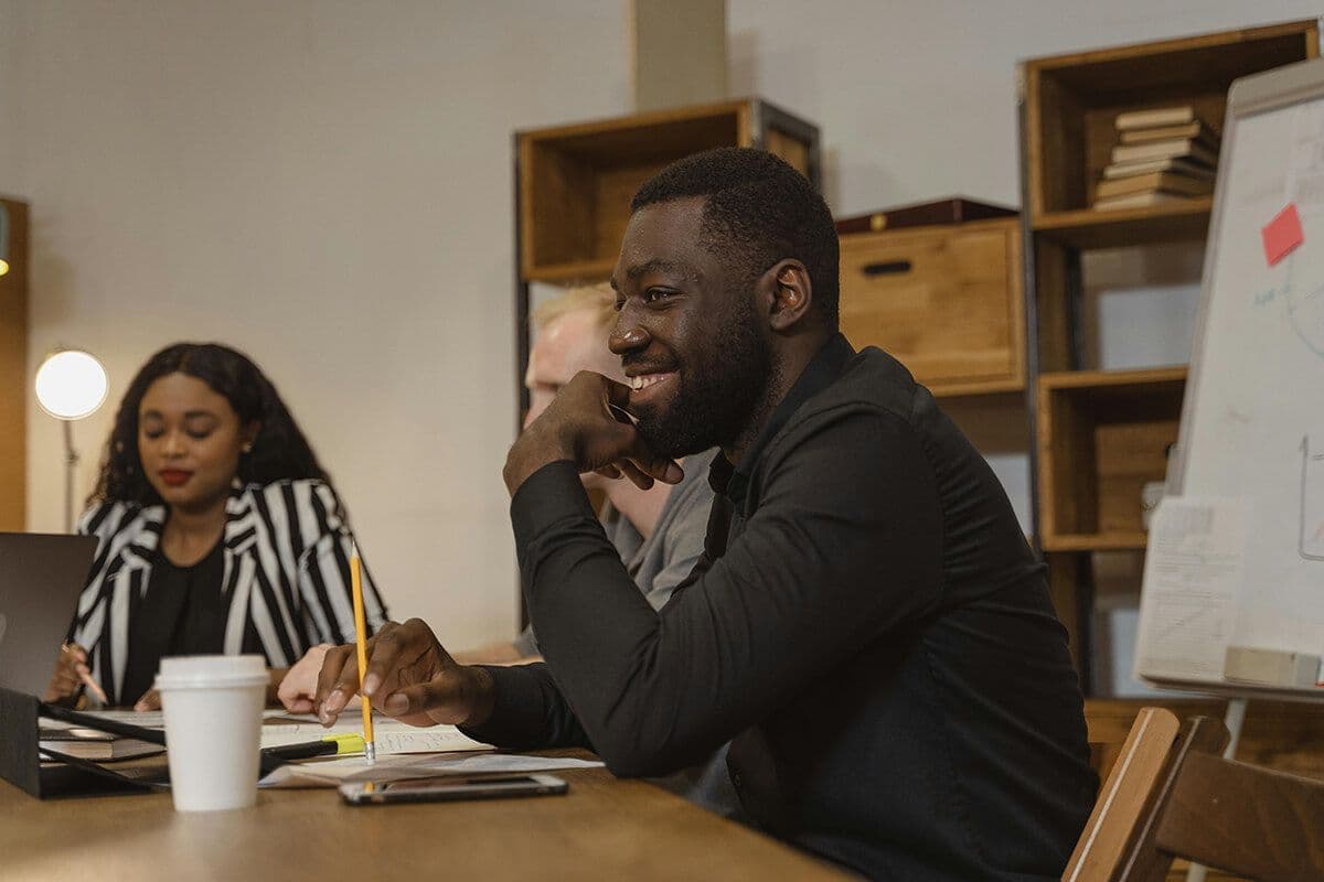 Man sitting at office table with co-workers, holding pencil and notebook while discussing leadership topics