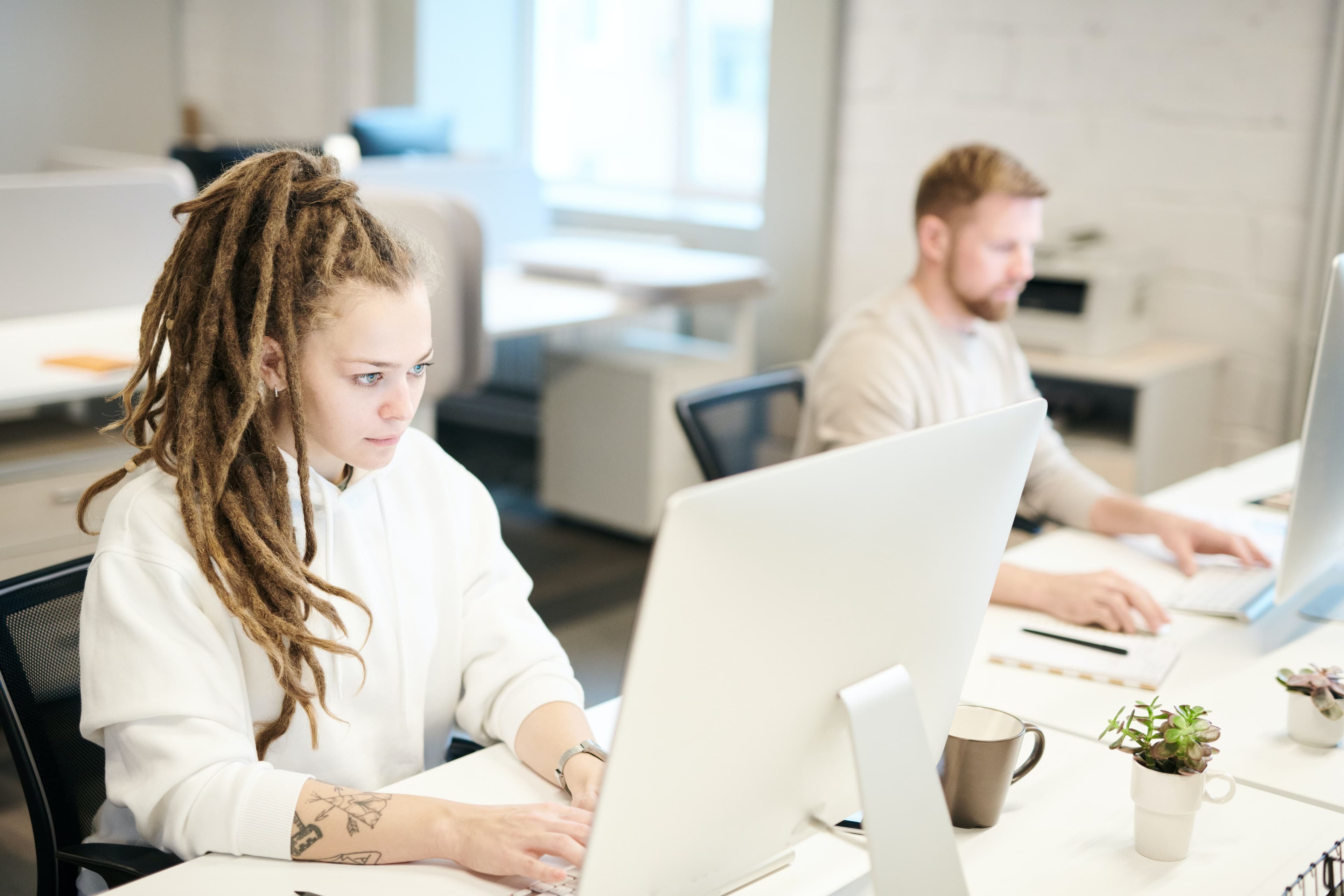 woman working at her computer in an office. Male colleague sits nearby.